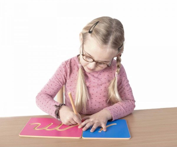 Une fille trace les lettres creusées Montessori - de l'écriture vers la lecture