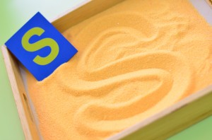 Tracer les lettres dans le sable en utilisant un modèle.